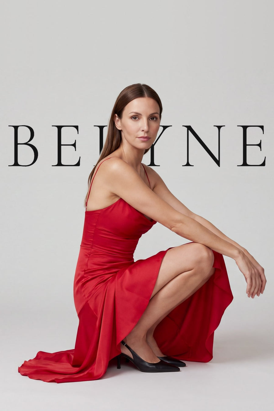 Femme accroupie en robe longue rouge en satin devant le logo Belyne